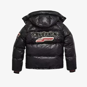 May include: Black puffer jacket with a hood. The jacket features the brand name "Avirex" in white and red lettering on the back, along with a patch that says "All Star Bombers". The jacket has a glossy finish.