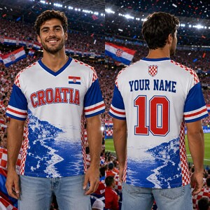 May include: A white, red, and blue soccer jersey featuring the text CROATIA on the front and YOUR NAME with the number 10 on the back. The design includes a red and white checkered pattern on the sides and a coastal landscape graphic.