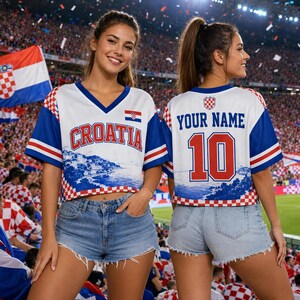 May include: A white, blue, and red V-neck crop top jersey featuring the text CROATIA on the front and YOUR NAME with the number 10 on the back. The design includes a red and white checkered pattern on the sleeves and hem, with a coastal landscape graphic.