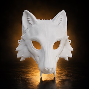 May include: A white wolf mask featuring pointed ears, almond-shaped eye openings, and a snout with two small fangs at the bottom. The mask has small circular holes on the sides for attachment and a smooth, matte finish across the entire surface.