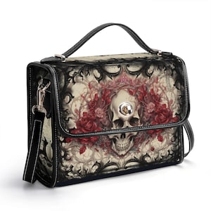 Peut inclure: Sac à main noir avec un motif de crâne entouré de roses rouges et de volutes noires. Il possède une poignée noire et une bandoulière amovible. Le motif est imprimé sur le devant, avec un fermoir argenté.
