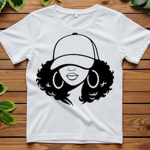 May include: White t-shirt featuring a black and white graphic of a woman wearing a baseball cap and hoop earrings. The design showcases a stylized face with curly hair, a cap, and large hoop earrings. The shirt is made of a soft, comfortable material.
