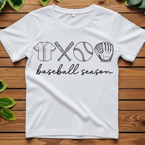 May include: White t-shirt with a black graphic of baseball equipment, including a jersey, crossed bats, a baseball, and a glove. The words "baseball season" are written in a cursive font below the graphic.