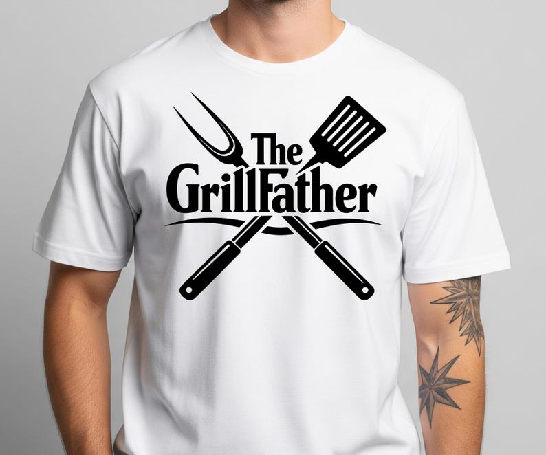 以下が含まれることがあります： 黒いグラフィックの白いTシャツ。グラフィックは、交差したグリルツールと「The Grillfather」のテキストを特徴としています。デザインにはヘラ、フォークが含まれており、テキストはツールのアーチ状になっています。