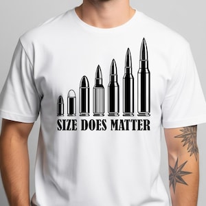 May include: White t-shirt featuring a black graphic of bullets increasing in size. The phrase "SIZE DOES MATTER" is printed beneath the bullets in a bold font. The t-shirt has a crew neck design and is made of a light fabric.