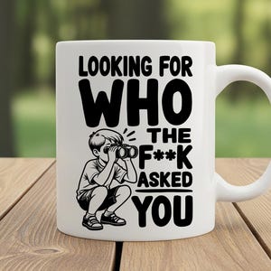 May include: White ceramic mug with a black graphic of a child looking through binoculars, and the text "LOOKING FOR WHO THE F*** ASKED YOU". The mug has a curved handle and is sitting on a wooden surface.
