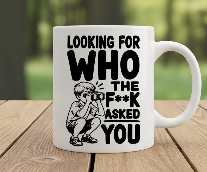 May include: White ceramic mug with a black graphic of a child looking through binoculars, and the text "LOOKING FOR WHO THE F*** ASKED YOU". The mug has a curved handle and is sitting on a wooden surface.