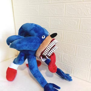 May include: A blue hedgehog plush toy with a large, open mouth displaying white teeth and a red tongue. The toy has white gloves, red shoes, and a black nose. The hedgehog is made of soft, blue fabric.