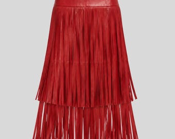 May include: A vibrant red leather skirt featuring a high-waisted design with a smooth waistband. The skirt is constructed with two distinct horizontal tiers of long, thin, vertical fringe that extend downward, creating a layered effect.