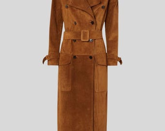 Puede incluir: Un abrigo largo tipo trench de ante marrón con diseño de doble botonadura, cinturón con hebilla rectangular y dos bolsillos delanteros. El abrigo presenta un cuello clásico, charreteras y puños abotonados. Mide unos 140 cm de largo.