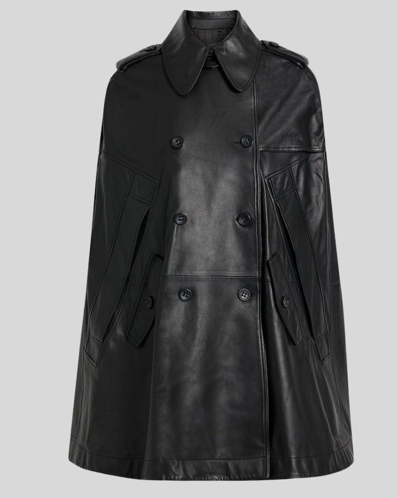 May include: A black leather cape with a double-breasted front, featuring large buttons and a classic collar. The cape has two front pockets and shoulder epaulettes. The garment is a stylish outerwear piece.