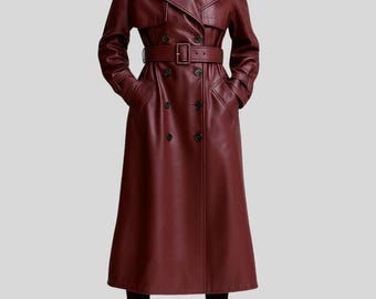 May include: A burgundy leather trench coat with a double-breasted front, a belted waist, and a classic collar. The long coat features a knee-length hem and long sleeves. The coat has a sleek, tailored design.