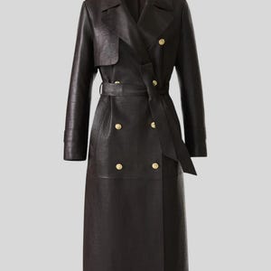 Könnte beinhalten: Langer, schwarzer Ledertrenchcoat mit doppelreihigem Design. Der Mantel hat einen Gürtel, goldfarbene Knöpfe und Schulterklappen. Ein klassisches Oberbekleidungsstück.