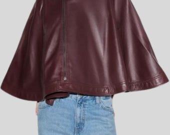 May include: A burgundy leather cape with a high collar and an asymmetrical zipper closure. The cape has a flowing, wide silhouette and is made of a smooth, shiny material. The garment is a stylish outerwear piece.