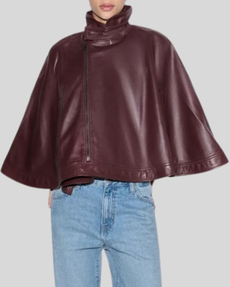 May include: A burgundy leather cape with a high collar and an asymmetrical zipper closure. The cape has a flowing, wide silhouette and is made of a smooth, shiny material. The garment is a stylish outerwear piece.