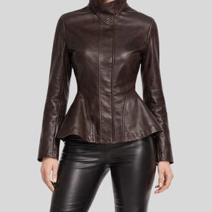 Könnte beinhalten: Braune Lederjacke mit Schößchen und hohem Kragen. Die Jacke hat einen Reißverschluss und lange Ärmel. Das Model trägt eine schwarze Lederhose.