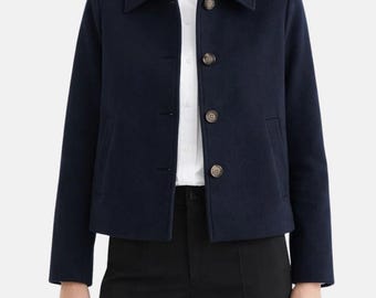 May include: A navy blue jacket with a classic collar and three brown buttons. The jacket has two front pockets and long sleeves. The model is wearing a white shirt and black pants.