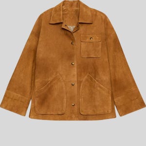 May include: A tan suede jacket with a collared neckline, button-down front, and two large front pockets. The jacket has long sleeves and a relaxed fit, perfect for layering. The jacket is a warm, earthy tone.