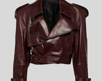 May include: A burgundy leather jacket with a classic trench coat design. Features include a notched collar, shoulder epaulets, a single-button closure, and a belt at the waist. The sleeves have adjustable cuffs with buckles. The jacket has a cropped length.