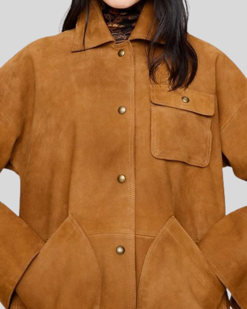 May include: A tan suede jacket with a collared neckline, button-down front, and two front pockets. The jacket has a relaxed fit and features gold-colored buttons. The overall style is casual and suitable for various occasions.