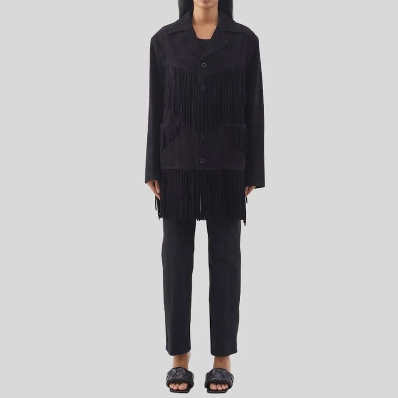 Puede incluir: Una chaqueta negra con flecos, combinada con pantalones negros a juego. La chaqueta tiene una botonadura frontal y dos bolsillos. Los flecos est&aacute;n en el pecho y en la parte inferior de la chaqueta. La modelo lleva sandalias negras.