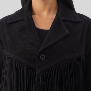 Puede incluir: Chaqueta negra de ante con detalles de flecos. La chaqueta presenta un cuello cl&aacute;sico, un cierre de un solo bot&oacute;n y un ribete de flecos en la parte delantera. La chaqueta es de color negro liso y parece estar hecha de un material suave similar al ante.