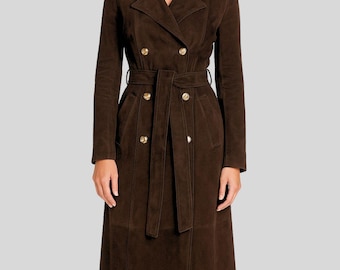 May include: A long, brown suede trench coat with a double-breasted design. The coat features gold-colored buttons, a matching belt, and a classic collar. The coat is knee-length and has long sleeves.