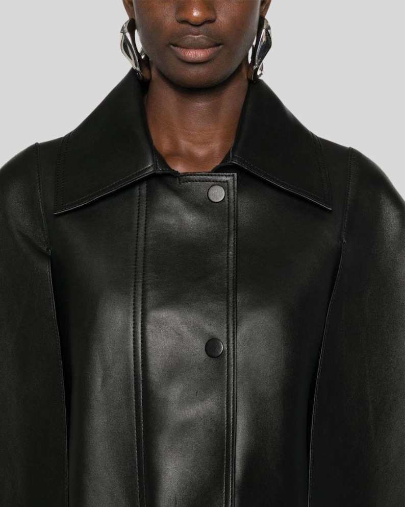 Puede incluir: Chaqueta de cuero negro con cuello ancho y dos botones visibles. La chaqueta tiene un corte entallado y un dise&ntilde;o elegante y minimalista, adecuado para diversas ocasiones.