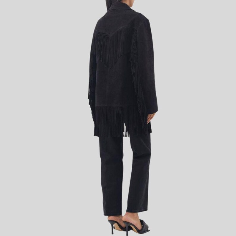 Puede incluir: Chaqueta de ante negra con flecos en la espalda y las mangas. La chaqueta se combina con pantalones negros y sandalias negras de tac&oacute;n alto. El conjunto es de estilo western.