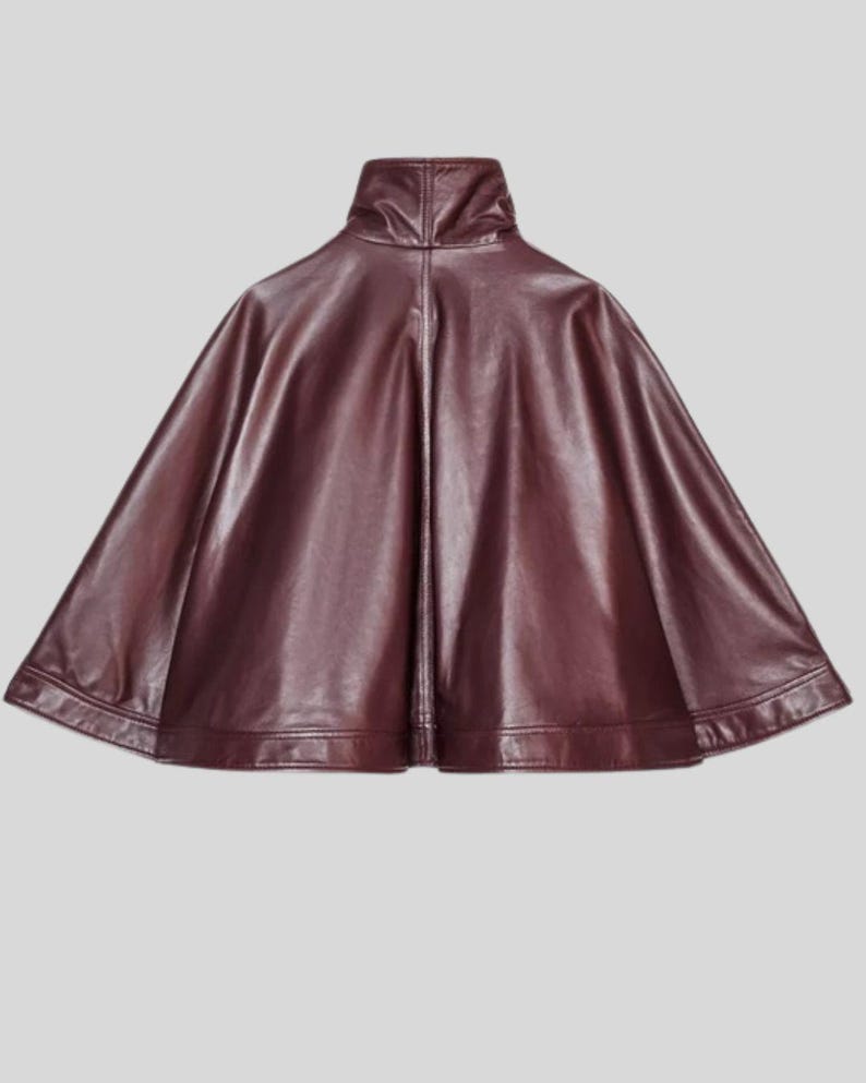 May include: A burgundy faux leather cape with a high collar. The cape has a smooth, shiny finish and a wide, flowing silhouette. The hemline is straight and the cape is designed to be worn over the shoulders.