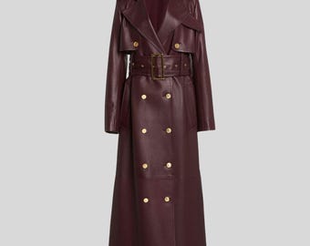May include: A full-length, burgundy leather trench coat. The coat features a double-breasted design with gold-colored buttons, a belted waist, and a notched collar. The coat has a classic trench coat silhouette.