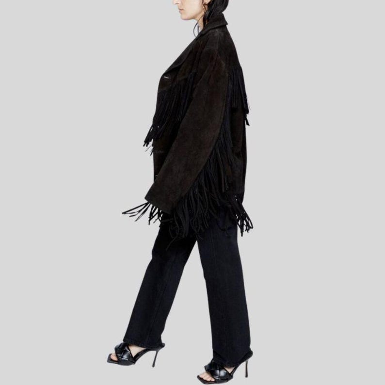 Puede incluir: Chaqueta de ante marr&oacute;n oscuro con flecos largos. Se combina con vaqueros negros y sandalias negras de tac&oacute;n alto. El conjunto se presenta sobre un fondo gris claro.