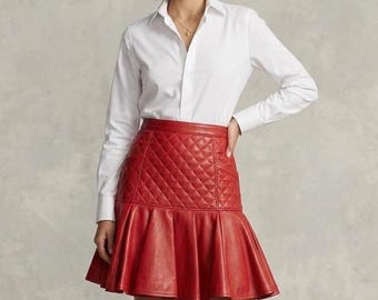 May include: A crisp white long-sleeved button-down shirt paired with a vibrant red leather skirt. The skirt features a quilted diamond-patterned upper section and a flared, pleated hemline that falls above the knee, creating a structured silhouette.