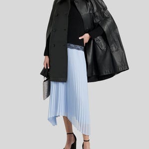 May include: A black leather cape coat with a matching black turtleneck sweater and a light blue pleated skirt. The outfit is accessorized with black platform heels and a small, silver, beaded handbag. The coat has a double-breasted design.