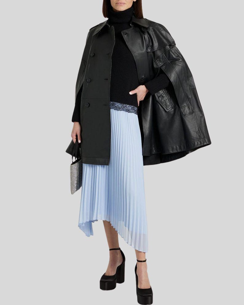 May include: A black leather cape coat with a matching black turtleneck sweater and a light blue pleated skirt. The outfit is accessorized with black platform heels and a small, silver, beaded handbag. The coat has a double-breasted design.