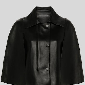 Puede incluir: Una chaqueta tipo capa de cuero negro con cuello cl&aacute;sico y cierre de botones en la parte delantera. La chaqueta presenta un dise&ntilde;o tipo capa con mangas cortas. La prenda est&aacute; hecha de un material liso y brillante.