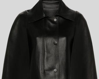 May include: A black leather cape jacket with a classic collar and button-down front. The jacket features a cape-style design with short sleeves. The garment is made of a smooth, shiny material.