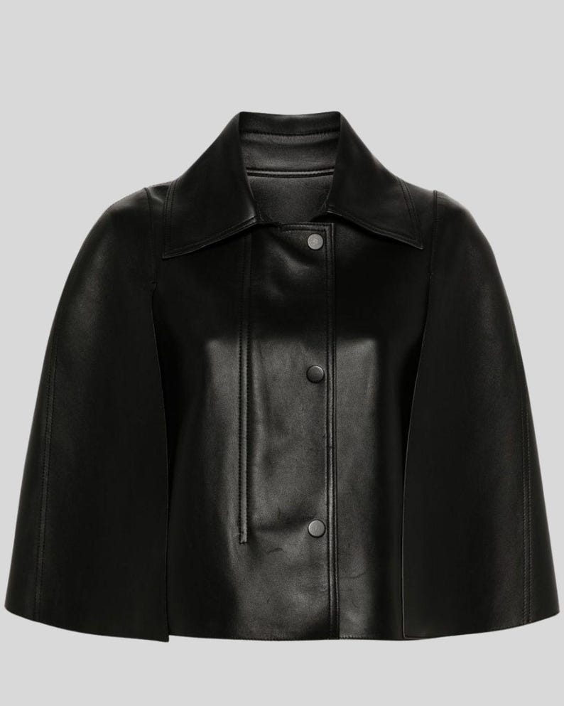 Puede incluir: Una chaqueta tipo capa de cuero negro con cuello cl&aacute;sico y cierre de botones en la parte delantera. La chaqueta presenta un dise&ntilde;o tipo capa con mangas cortas. La prenda est&aacute; hecha de un material liso y brillante.