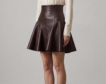 May include: A long-sleeve cream-colored blouse with a round neckline and a front button placket, paired with a high-waisted dark brown leather skirt featuring a flared hemline and vertical seam detailing, and dark brown leather ankle boots.