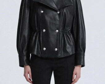 May include: A black leather jacket with a high collar and silver buttons. The jacket has a double-breasted design and a cinched waist. The model is wearing black pants. The jacket is a stylish outerwear piece.