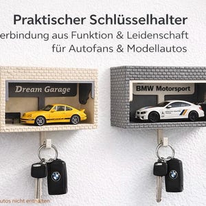 May include: Two key holders shaped like miniature garages, one beige and one gray, each with a toy car inside. The beige garage has a yellow car and the text "Dream Garage". The gray garage has a white car and the text "BMW Motorsport".