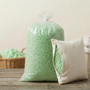 Può includere: Un grande sacco di plastica trasparente pieno di perline di schiuma verde, accanto a un cuscino beige con una cerniera aperta che rivela lo stesso ripieno verde. Un cesto di vimini con altre perline verdi è sullo sfondo.