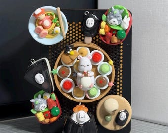 May include: A black display board featuring various miniature clay food charms. The collection includes bowls of noodles, bento boxes with cartoon characters, a central tray with a white mouse surrounded by small colorful treats, and black ghost figures.