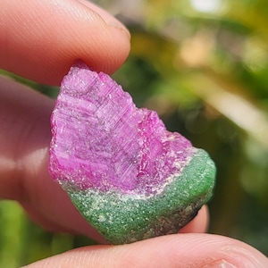 May include: A raw, unpolished mineral specimen featuring a vibrant magenta-pink crystalline upper section with distinct geometric facets and a contrasting opaque, textured forest-green base, showcasing natural colour zoning and crystalline structure.