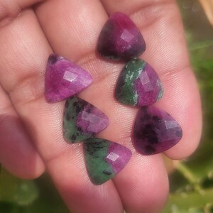 Peut inclure: Plusieurs pierres précieuses triangulaires facettées. Les pierres présentent un mélange de magenta profond et de vert, avec une surface polie et réfléchissante. Les pierres sont disposées en cercle, mettant en valeur leurs variations de couleurs uniques.