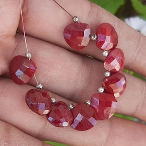 May include: A strand of faceted, heart-shaped, deep red gemstones. Each gem is connected by a thin, silver-colored wire and small silver beads. The gems have a sparkling, polished appearance.