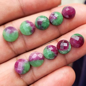 Può includere: Una collezione di dieci pietre preziose rotonde e sfaccettate con una distinta combinazione di colori di rubino magenta vibrante e zoisite verde opaca. Ogni pietra mostra un motivo unico di questi due colori, lucidato con una finitura liscia.