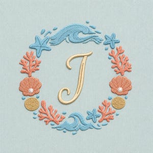 Op de afbeelding: Geborduurd ontwerp met een gouden letter "J" omringd door een krans van oceaan elementen. De krans bevat blauwe golven, zeesterren, koraal en schelpen in oranje en goud, tegen een lichtblauwe achtergrond.