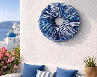 May include: A round, decorative wall art piece with a blue and white striped design. The art is mounted on a white wall, with a view of a coastal landscape in the background. The piece has a circular shape with a hole in the center.