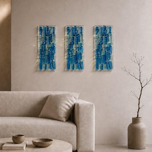 May include: Three rectangular wall art panels featuring a mosaic of vertical glass pieces in varying shades of deep blue and light turquoise. Each panel is composed of numerous small, rectangular glass segments arranged in a grid-like pattern.